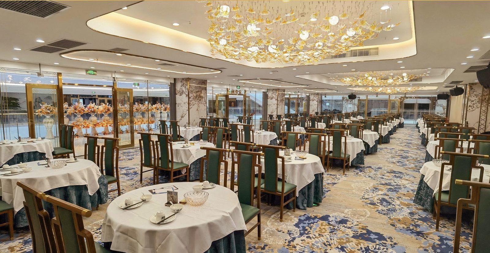 A banquet hall with round tables, green chairs, and a chandelier.