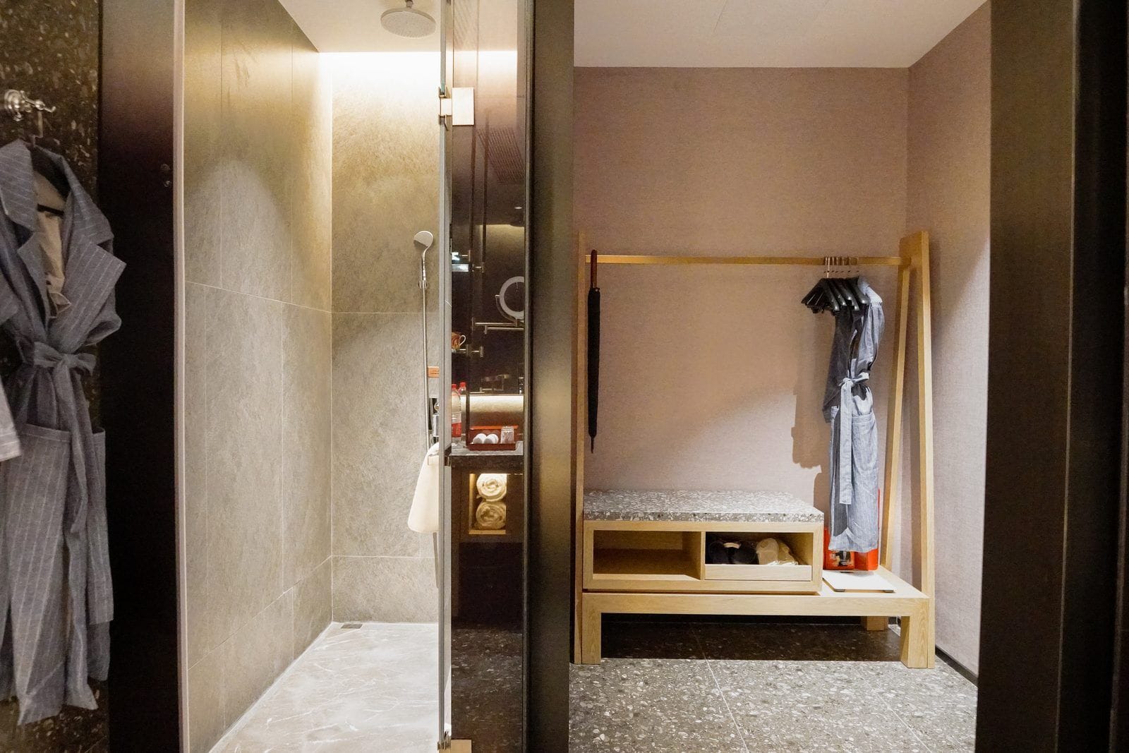 A modern bathroom with a shower, a robe rack, and a bench.
