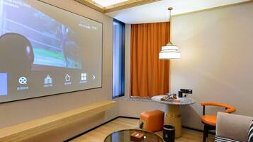 A hotel room with a projection screen displaying a movie, a round table with a lamp, a sofa, and a small trash bin.