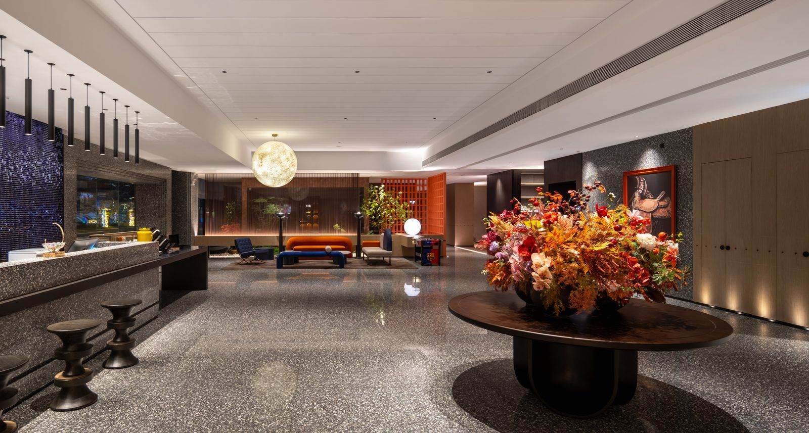 Un vestíbulo moderno con una zona de estar central, una recepción y un arreglo floral decorativo.