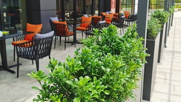 An outdoor seating area with chairs and tables, surrounded by planters with greenery.