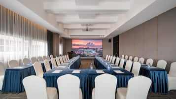 A conference room with a long table, white chairs, and a large screen displaying a cityscape.