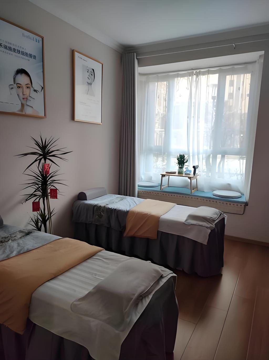 A hotel room with two beds, a large window with curtains, a small table with a plant, and framed pictures on the wall.