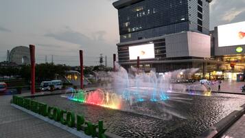 A water fountain with multiple jets and colorful lights in front of a modern building with a large billboard.