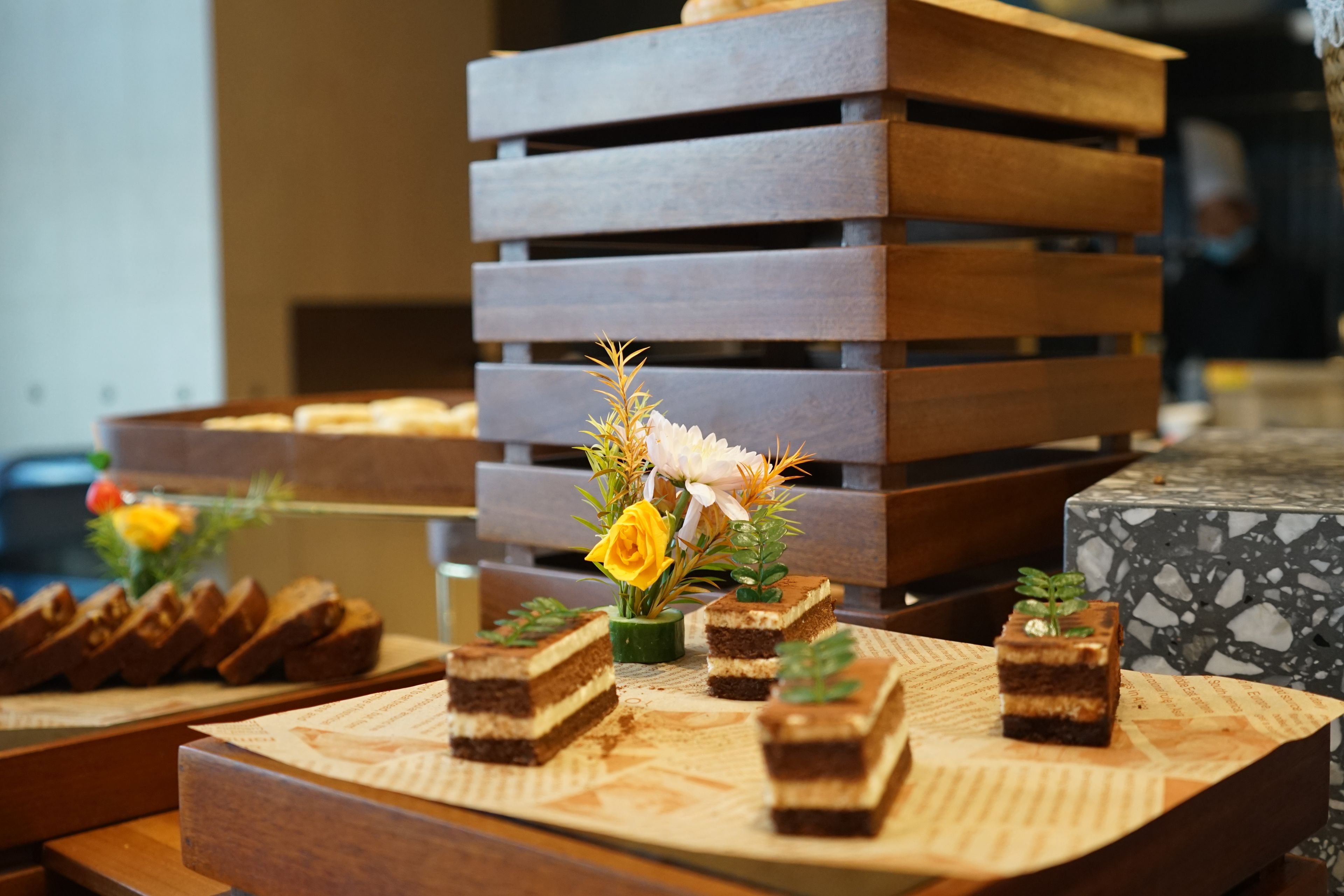 A dessert display with various cakes and a floral arrangement on a wooden table.