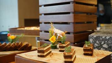 A dessert display with various cakes and a floral arrangement on a wooden table.