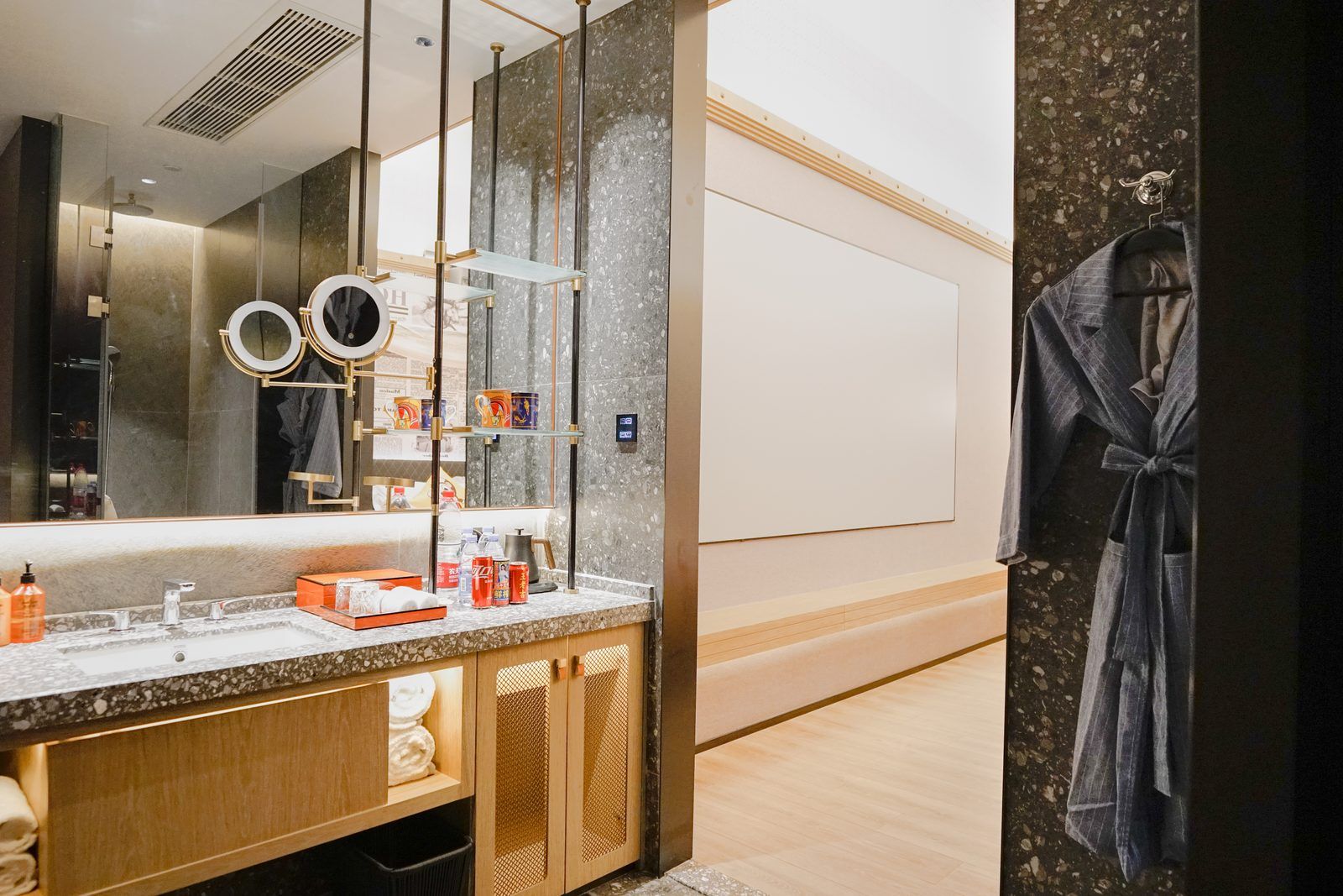 A modern bathroom with a large mirror, a vanity with a marble countertop, and a robe hanging on a hook.