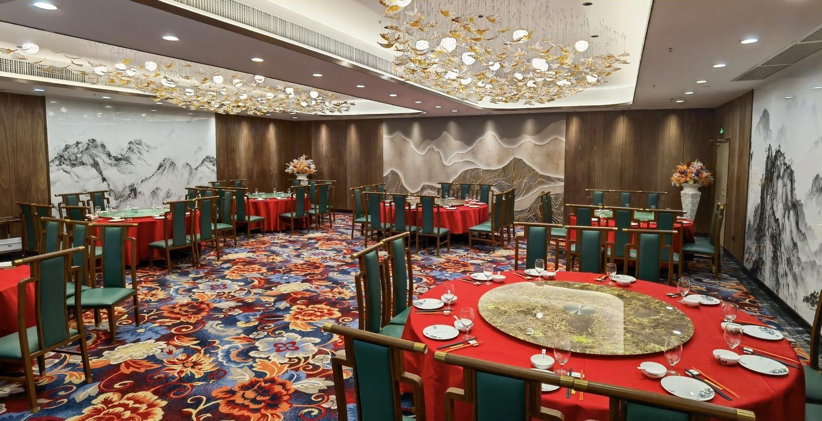 A banquet hall with round tables, green chairs, and red tablecloths.
