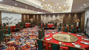 A banquet hall with round tables, green chairs, and red tablecloths.