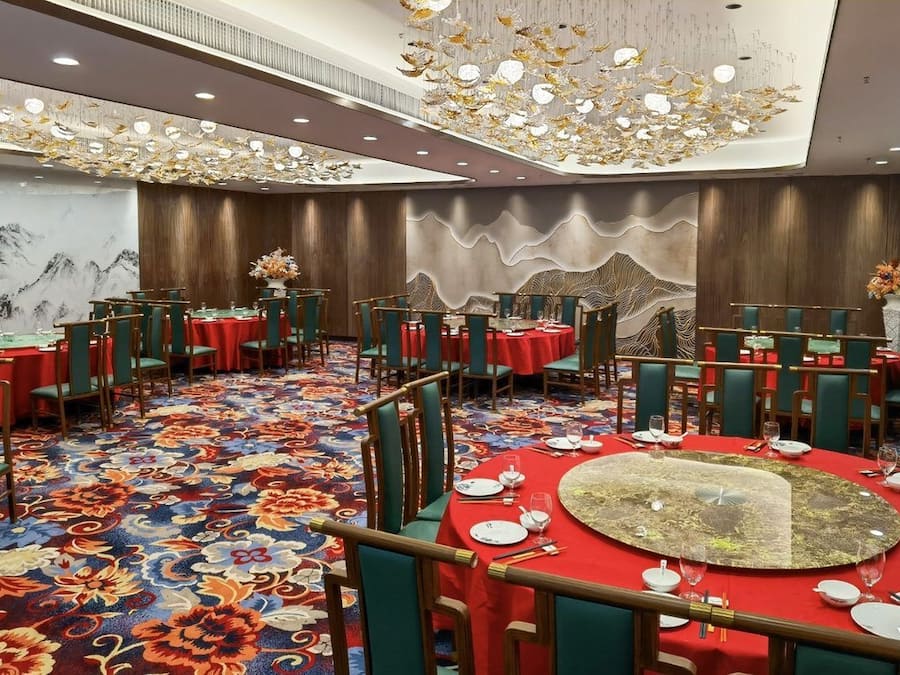 A banquet hall with round tables, green chairs, and red tablecloths.
