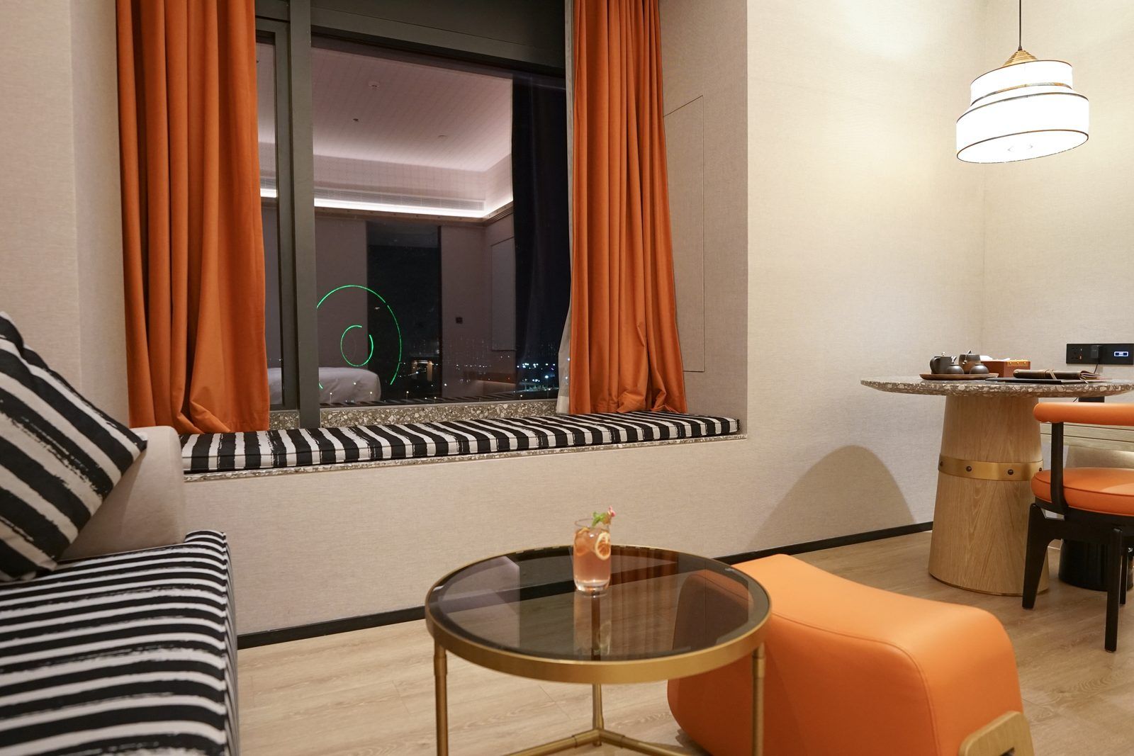 A modern room with a sofa, a round glass table, a dining table with chairs, and a window with curtains.