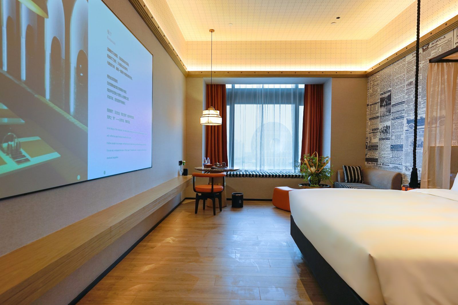 Habitación de hotel con cama, escritorio, silla, pantalla grande y ventana con cortinas.