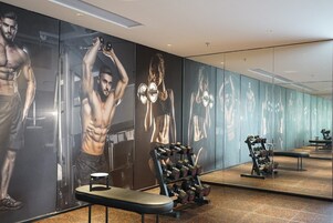 Un gimnasio con equipo de ejercicio y amplios espejos que reflejan el ambiente.