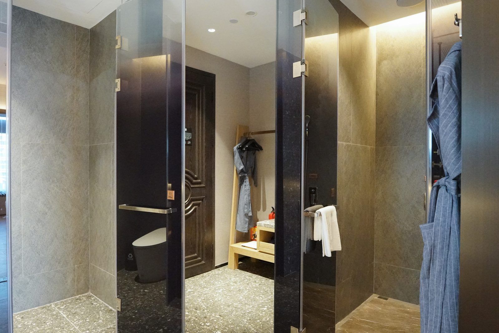 A modern bathroom with a glass partition, a shower area, a bench, and a robe hanging on a rack.