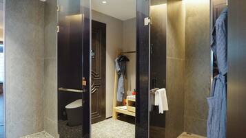 A modern bathroom with a glass partition, a shower area, a bench, and a robe hanging on a rack.
