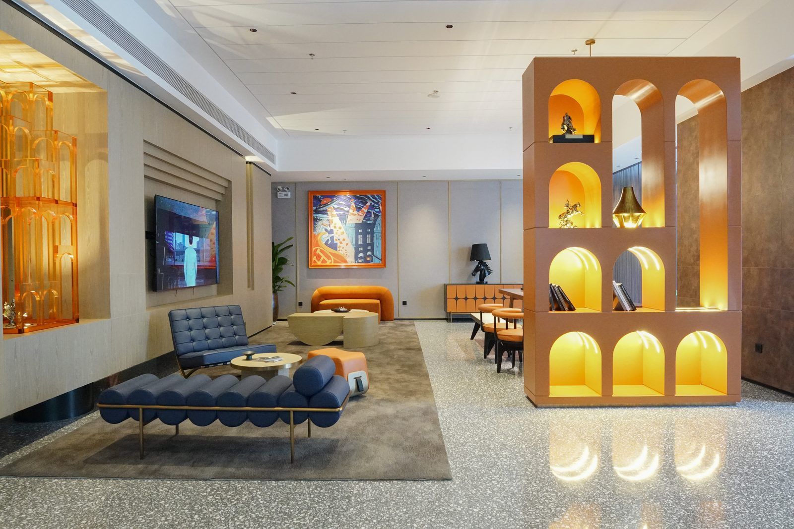A modern hotel lobby with a seating area, a large TV screen, and a unique illuminated display unit.