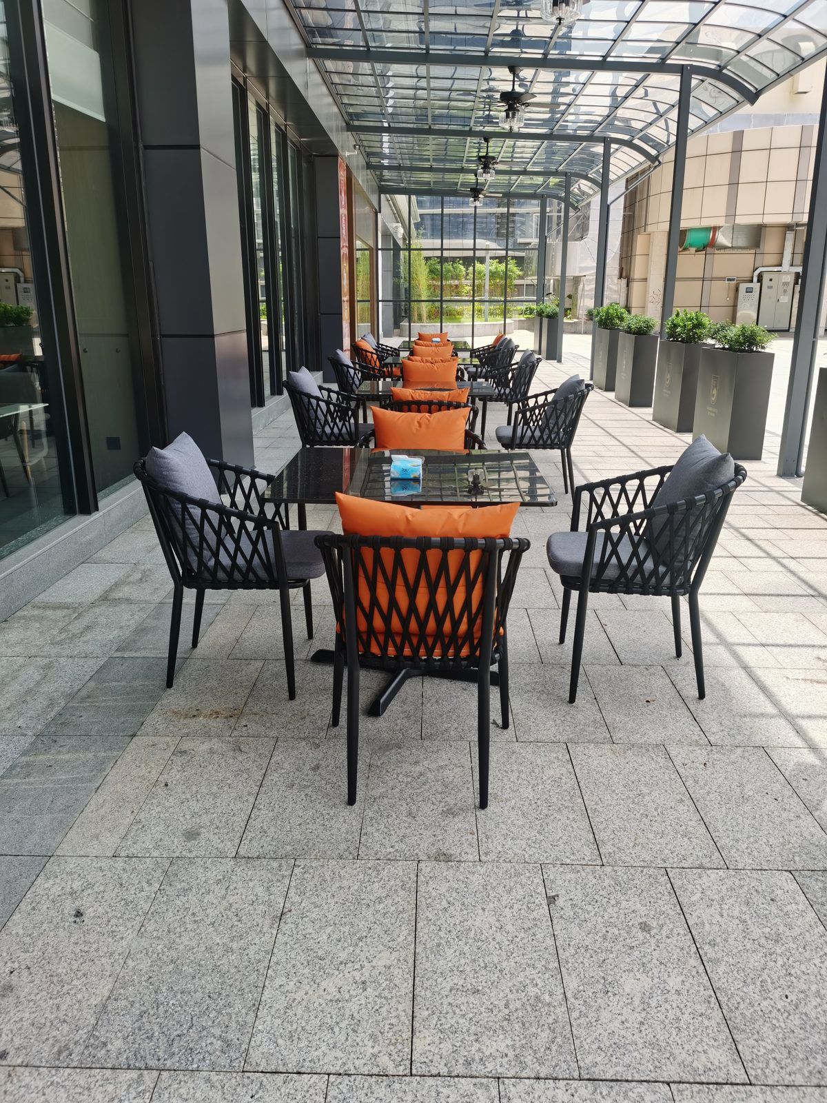 Un área de estar al aire libre con una mesa y sillas de vidrio, rodeada por un recinto de cristal.