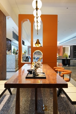 Um interior moderno com uma longa mesa de madeira, detalhes em laranja e uma escultura decorativa.