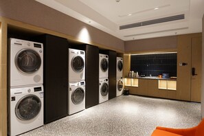 Un cuarto de lavandería con varias lavadoras, un lavamanos y un bote de basura.