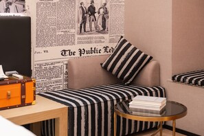 Habitación con sofá, almohada a rayas, una mesita redonda con libros y una pared decorada con periódicos.