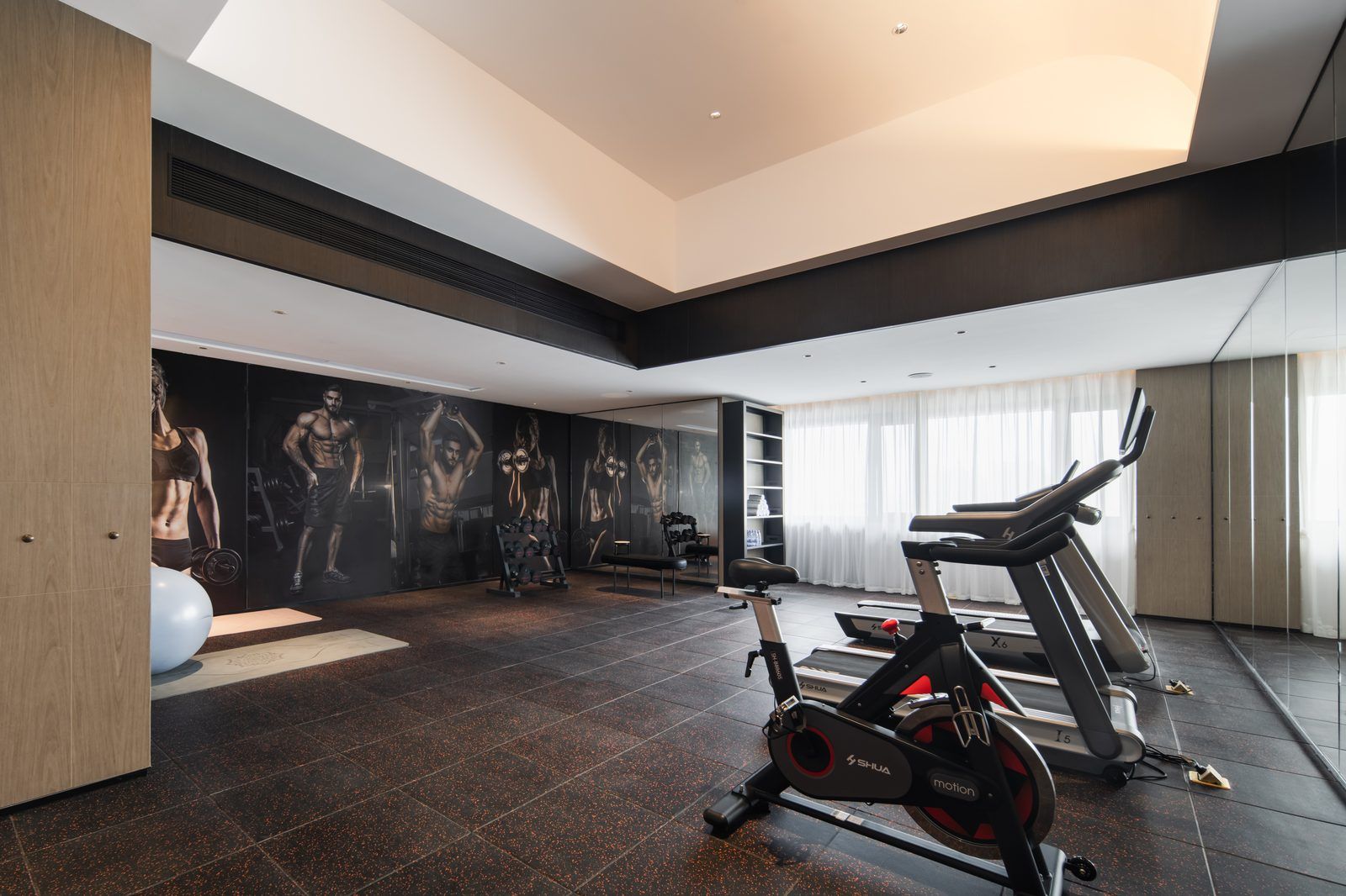 A modern gym with exercise equipment, a large mirror, and a wall with fitness images.