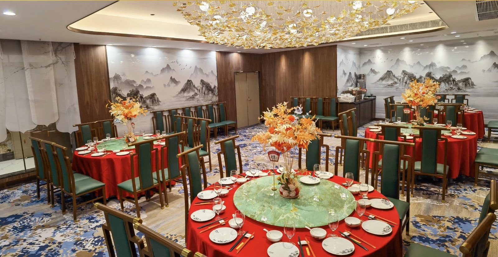 Un salón de banquetes con mesas redondas, sillas verdes y manteles rojos.