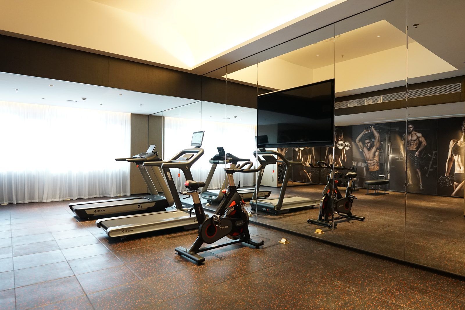 Una palestra con tapis roulant, cyclette e uno specchio che riflette gli attrezzi da allenamento.