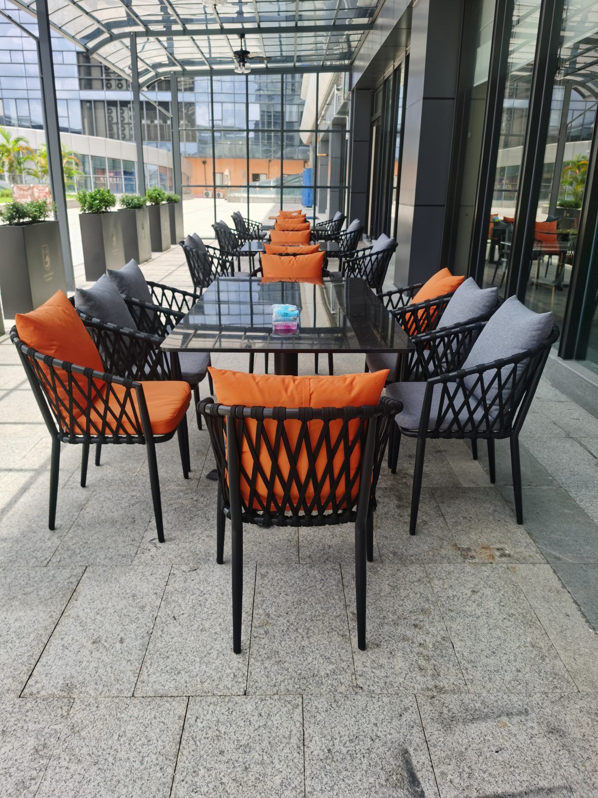 An outdoor patio with a glass-top table surrounded by wicker chairs with orange cushions.