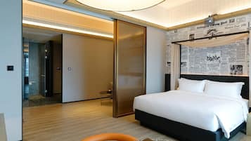Habitación de hotel con cama, escritorio y silla. Se ve una puerta que conduce a otra habitación y una pared con recortes de periódico.