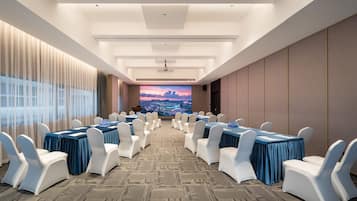 A conference room with tables and chairs, a large screen, and a view of a cityscape.