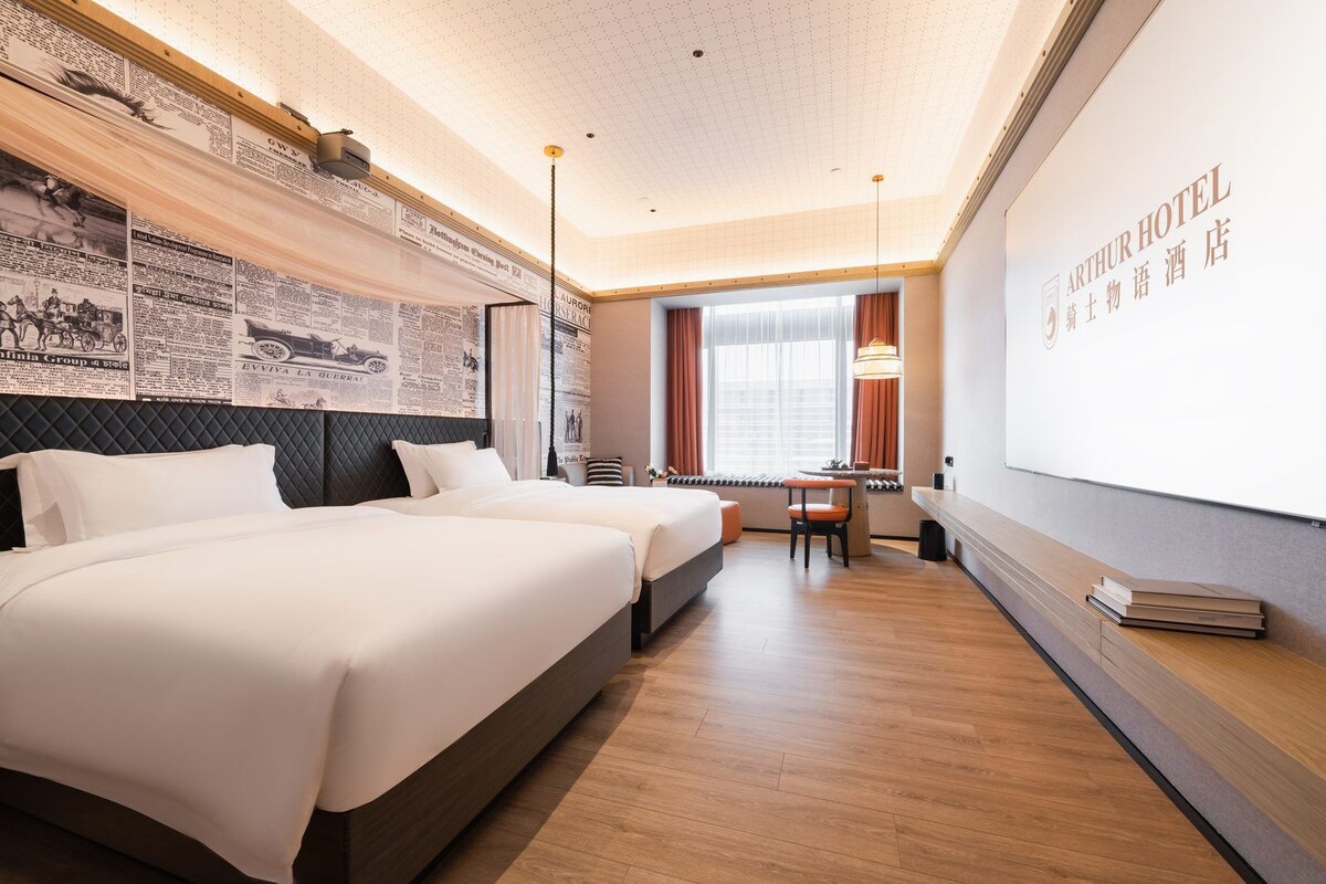 Habitación de hotel con dos camas, un escritorio y un ventanal grande.