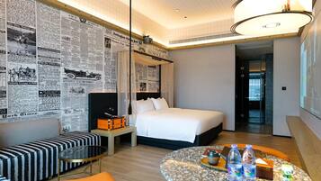 A hotel room with a bed, a seating area with a table, and a wall covered with newspaper clippings.