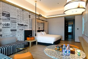 A hotel room with a bed, a seating area with a table, and a wall covered with newspaper clippings.