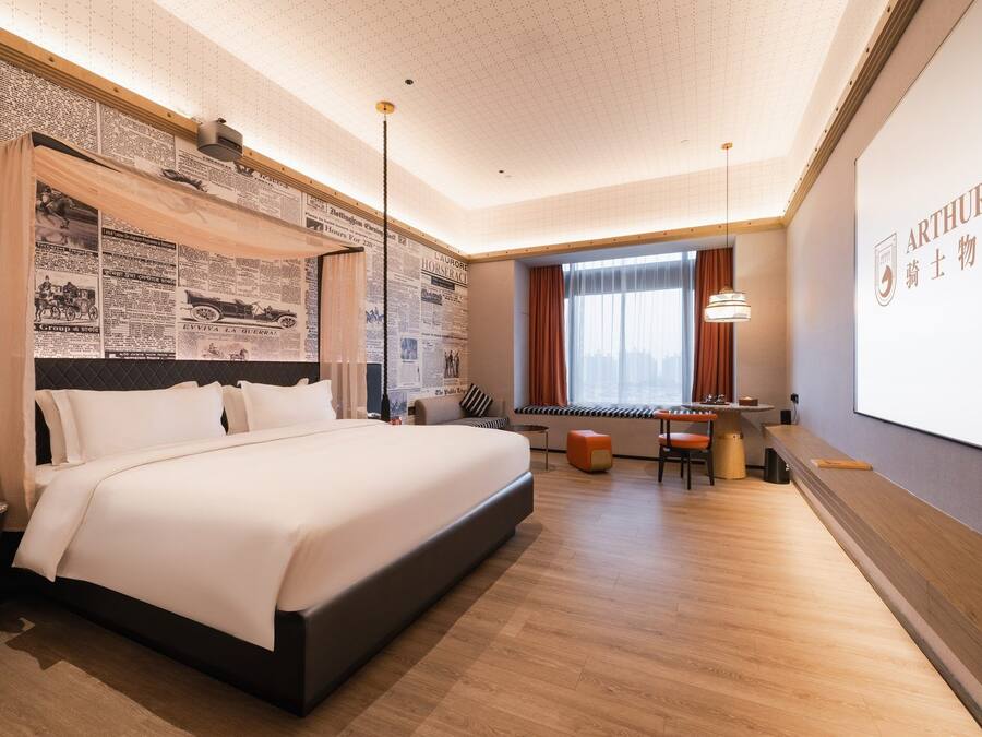 Een hotelkamer met een groot bed, een bureau en een projectiescherm waarop de naam van het hotel staat.