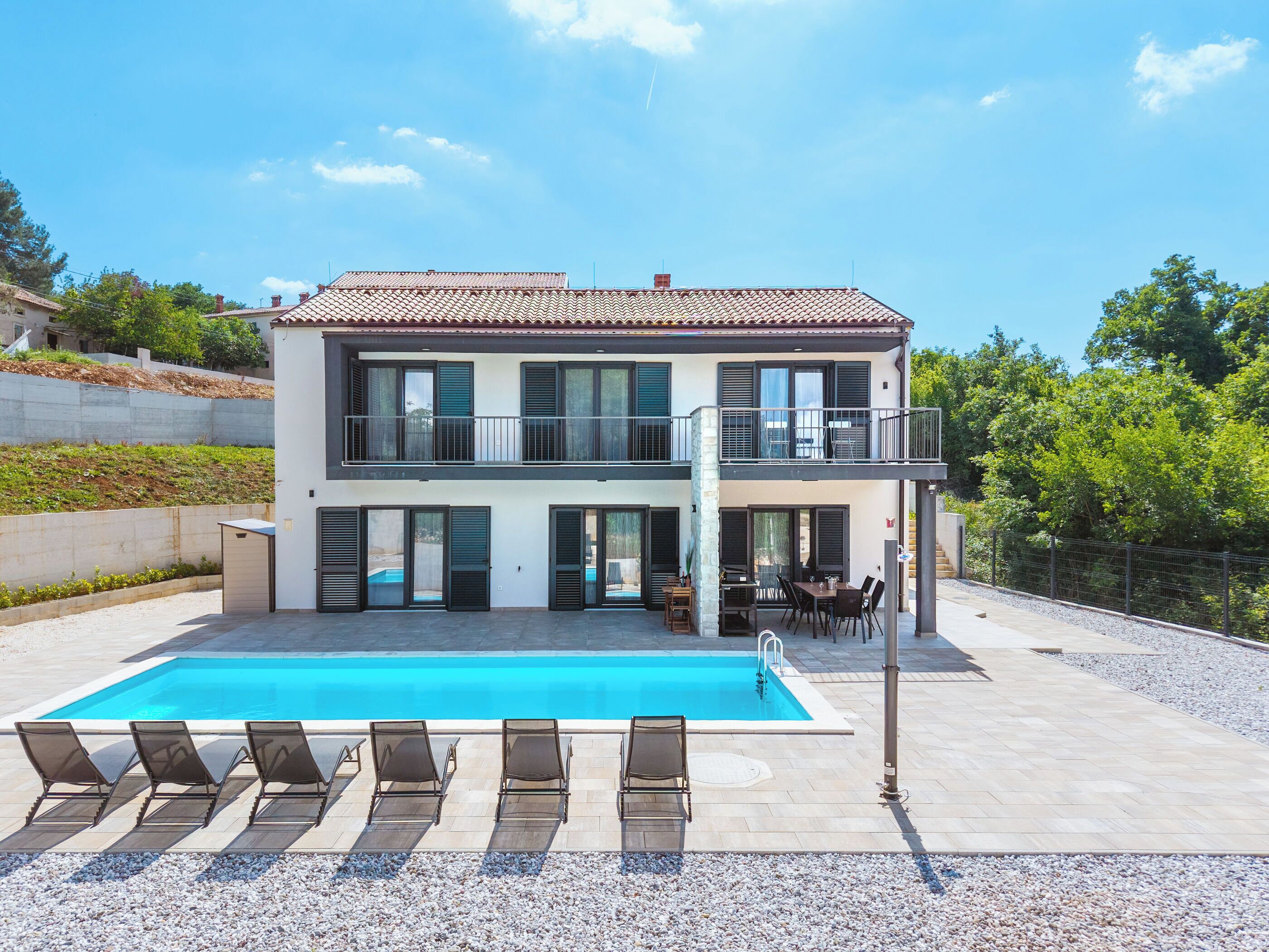 A two-story house with a swimming pool, outdoor seating, and a view of the surrounding area.