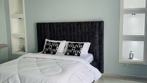 Una cama bien tendida con un cabecero oscuro y dos almohadones decorativos.