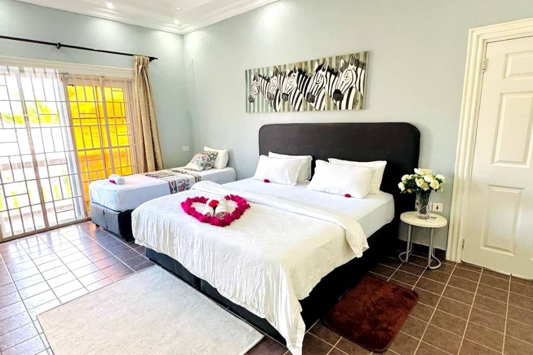 A bedroom with a large bed, a smaller bed, a window with curtains, a zebra artwork on the wall, and a door.