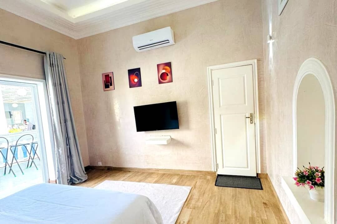 Quarto de hotel com cama, TV de tela plana, ar condicionado, porta e janela com cortinas.
