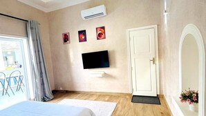 Habitación de hotel con cama, televisor de pantalla plana, equipo de aire acondicionado, puerta y ventana con cortinas.