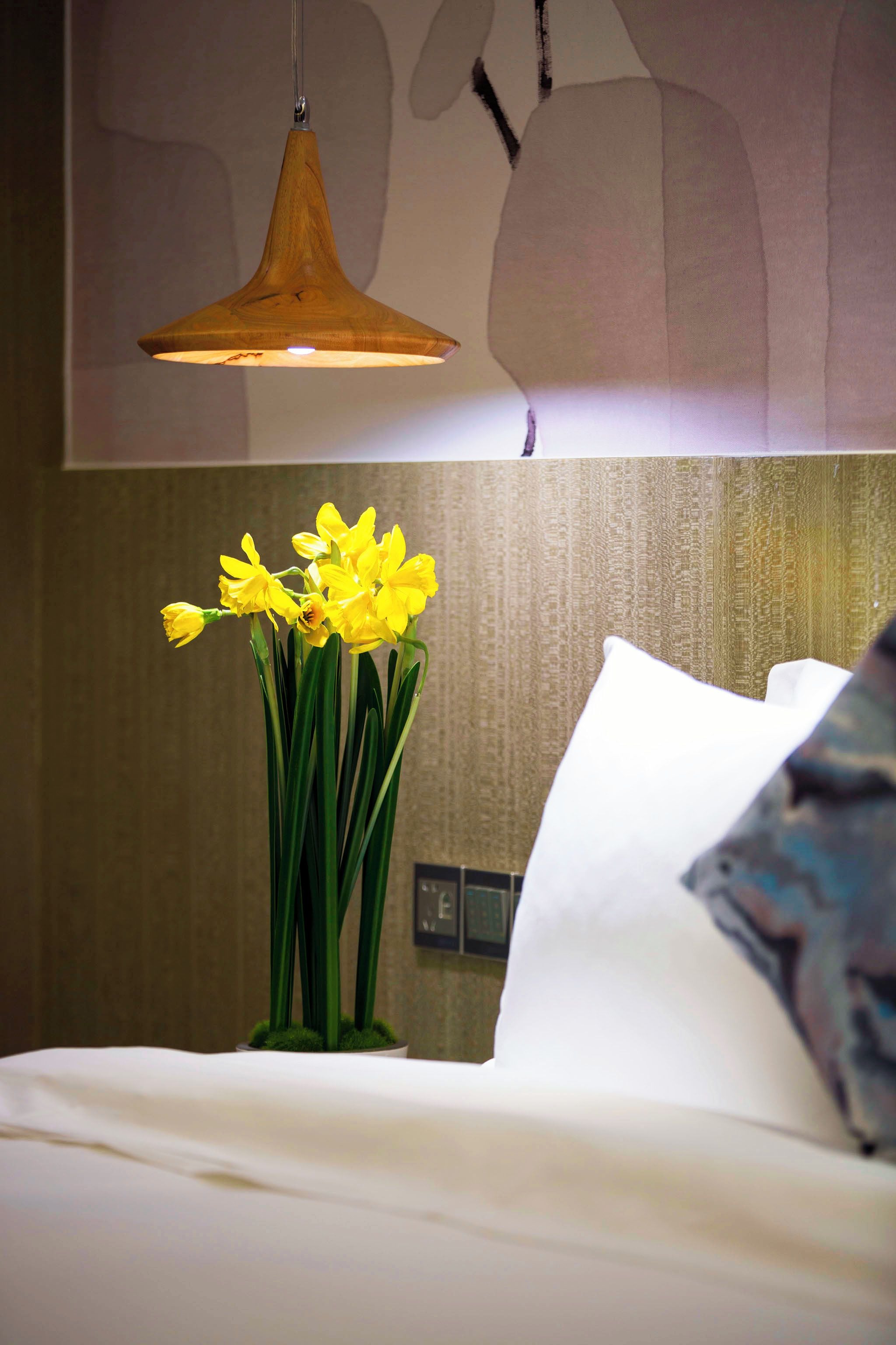 A bed with white bedding and a vase of yellow flowers.