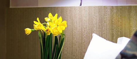 A bed with white bedding and a vase of yellow flowers.