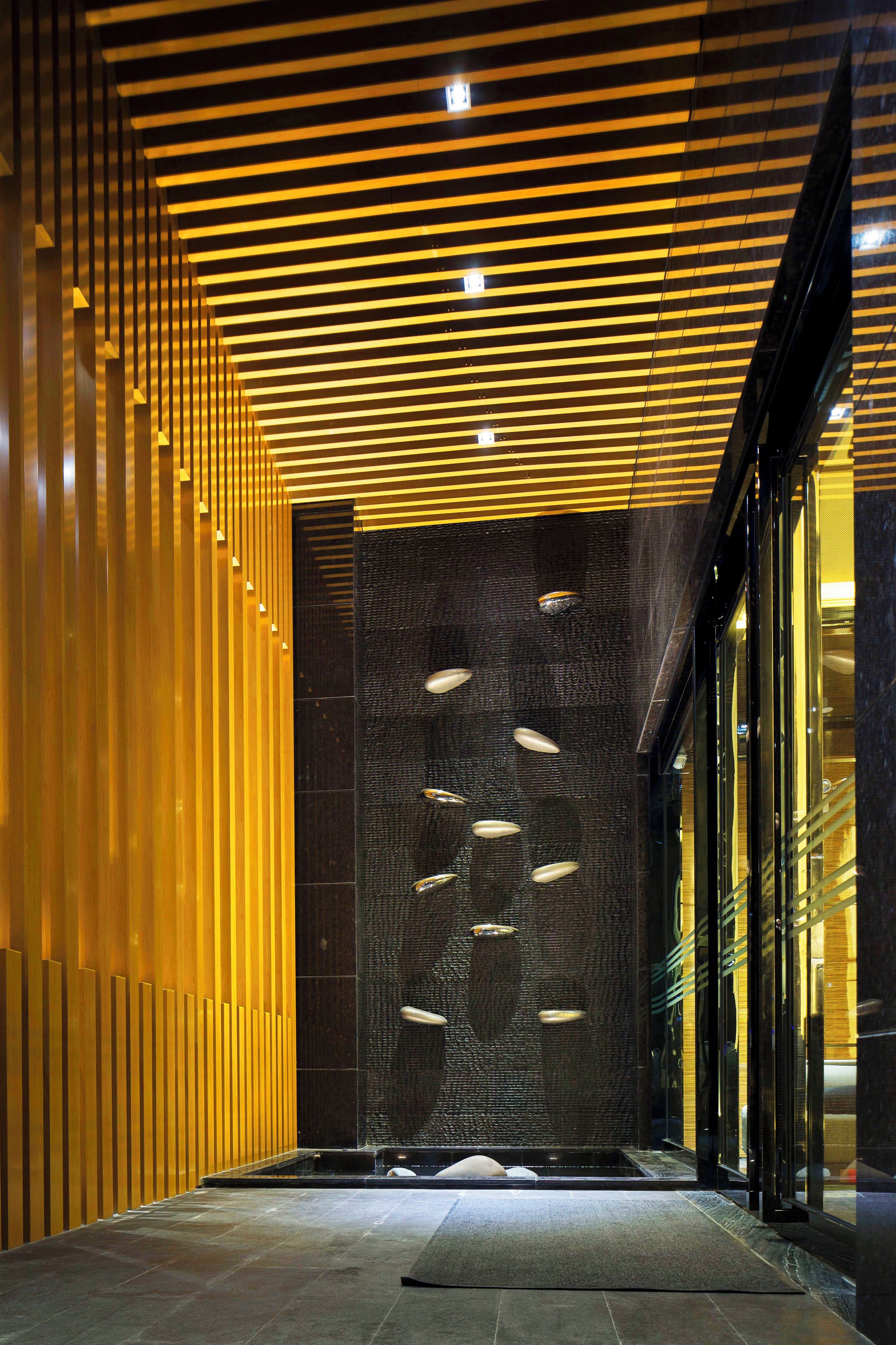 A modern interior with a wooden slatted wall, a textured wall with embedded lights, and a glass entrance.