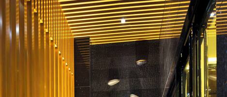 A modern interior with a wooden slatted wall, a textured wall with embedded lights, and a glass entrance.