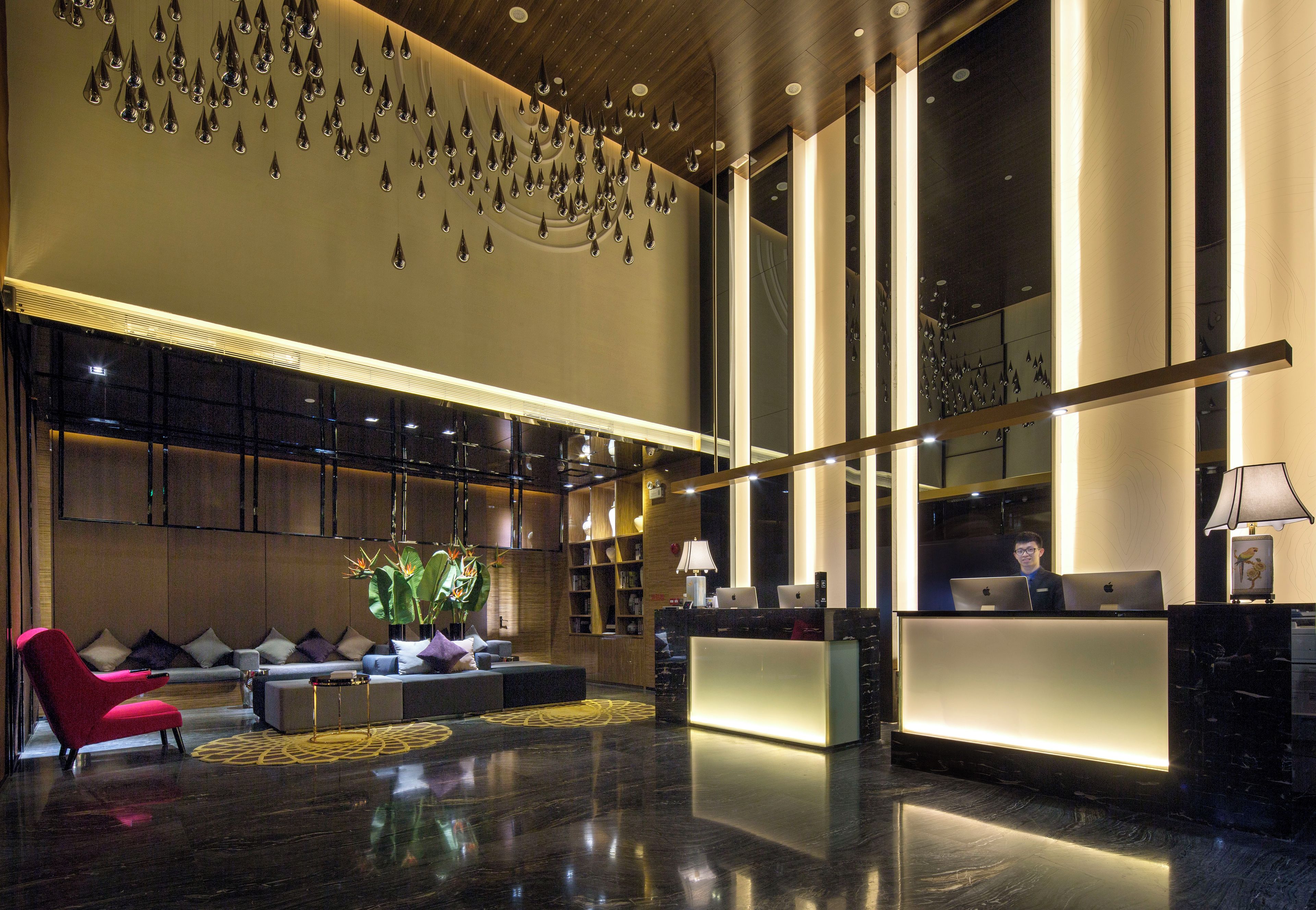 Een moderne lobby met een receptiebalie, een zithoek en decoratieve elementen aan het plafond.