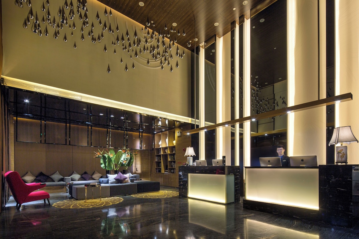 Um lobby moderno com balcão de recepção, área de estar e detalhes decorativos no teto.