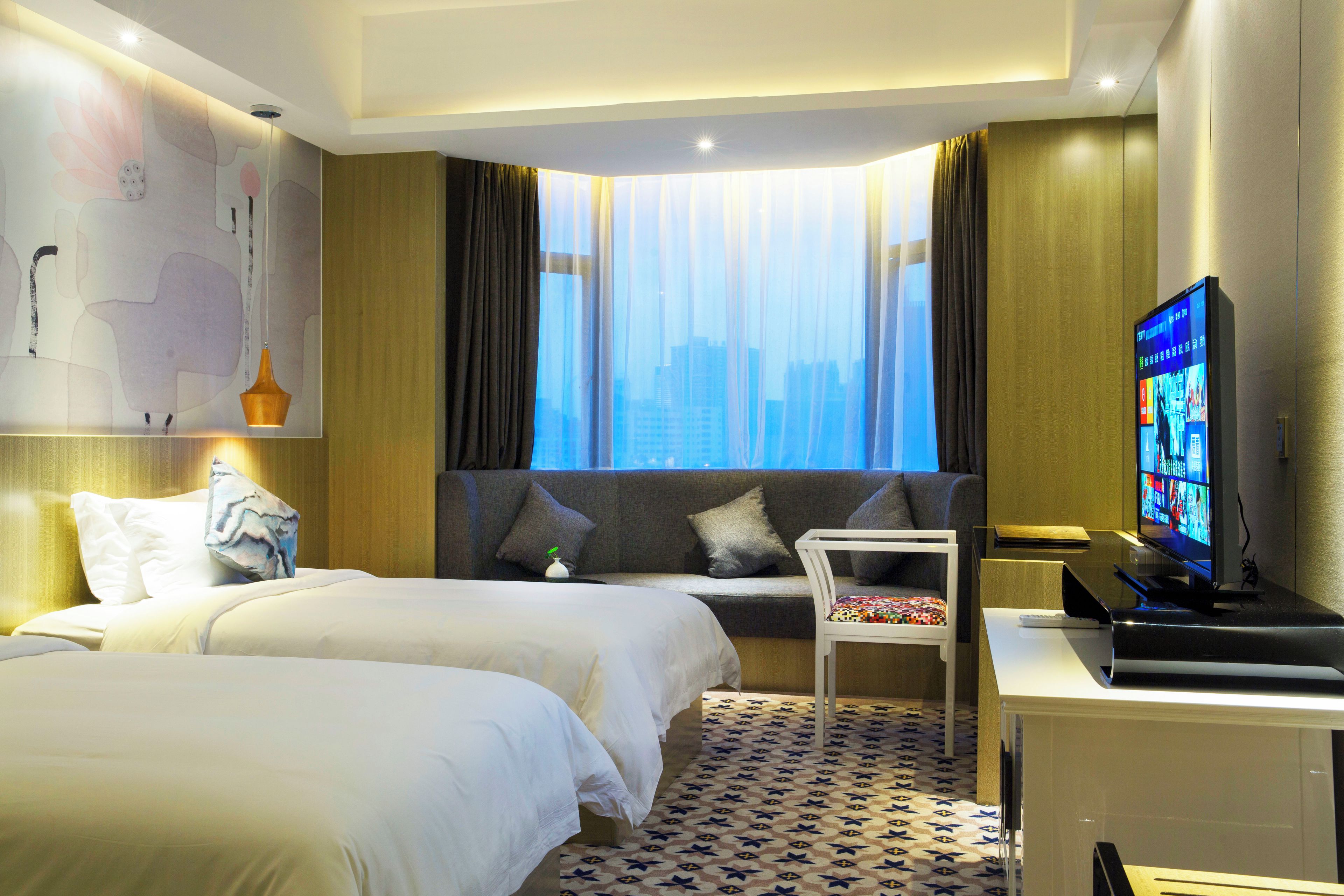 A hotel room with two beds, a TV, a desk, and a view of the cityscape.
