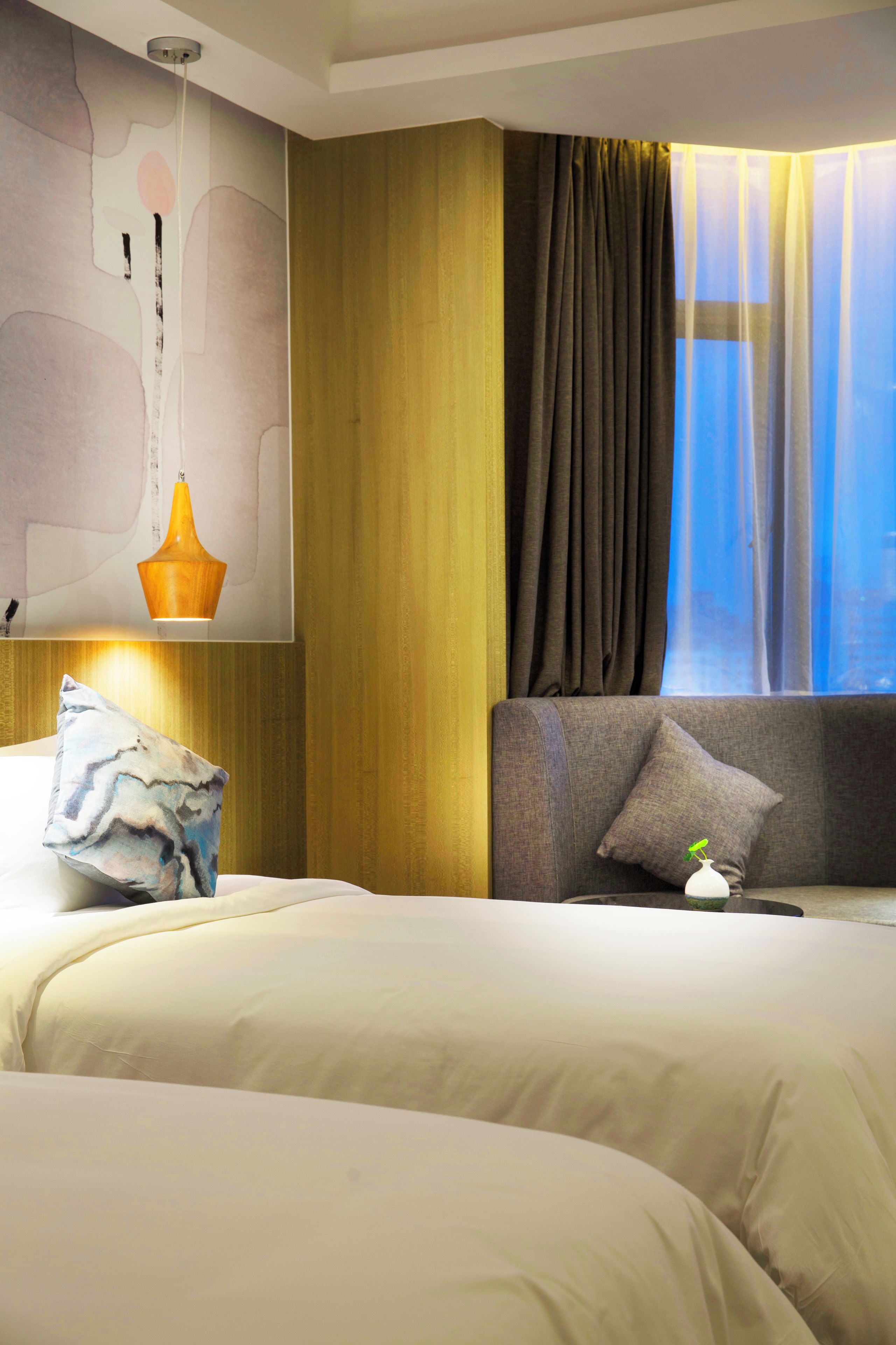 Quarto de hotel com uma cama grande, mesa de cabeceira, abajur e janela com cortinas.