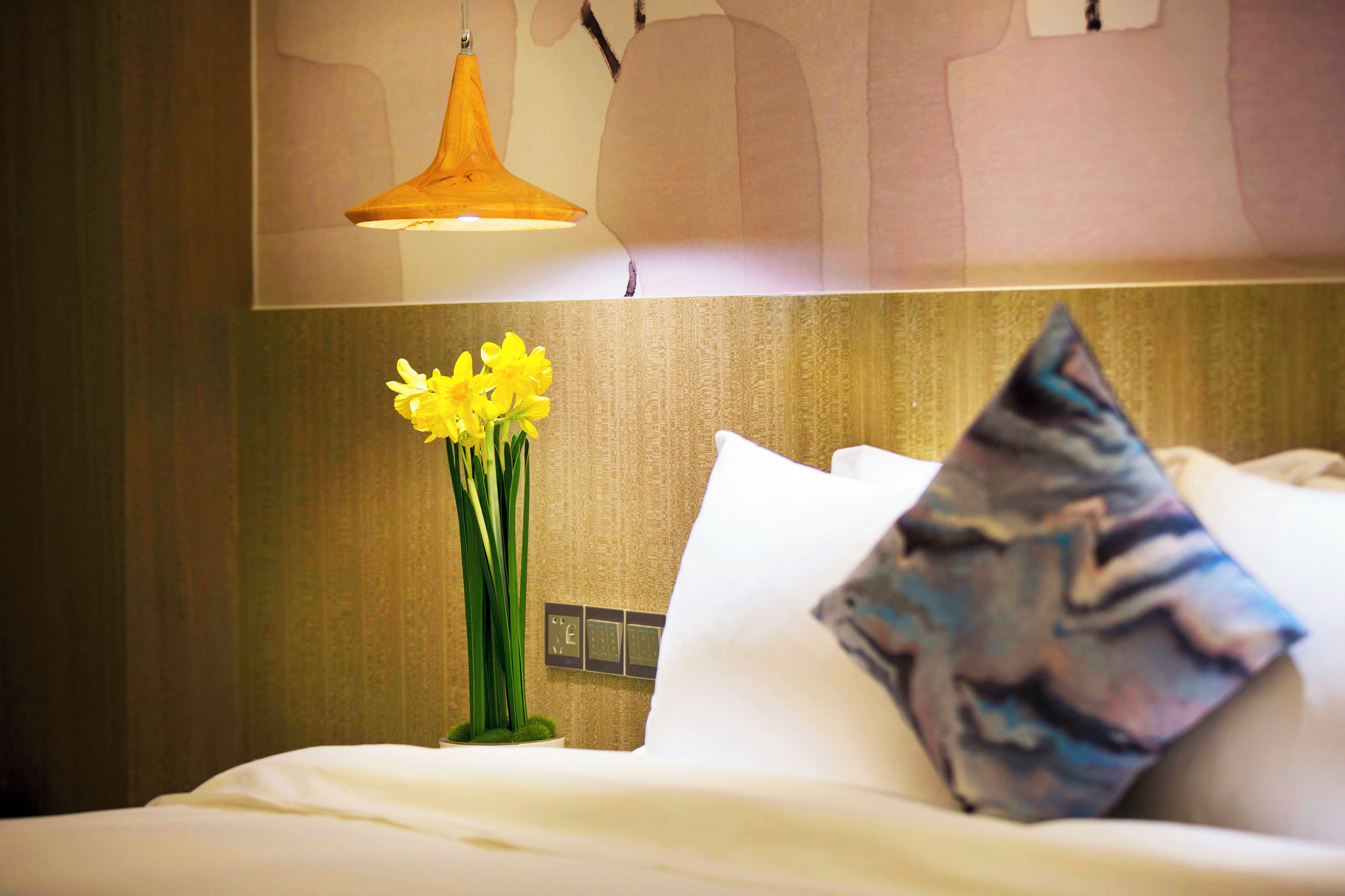 Habitación de hotel con cama, mesita de noche con un florero y una lámpara de pared.