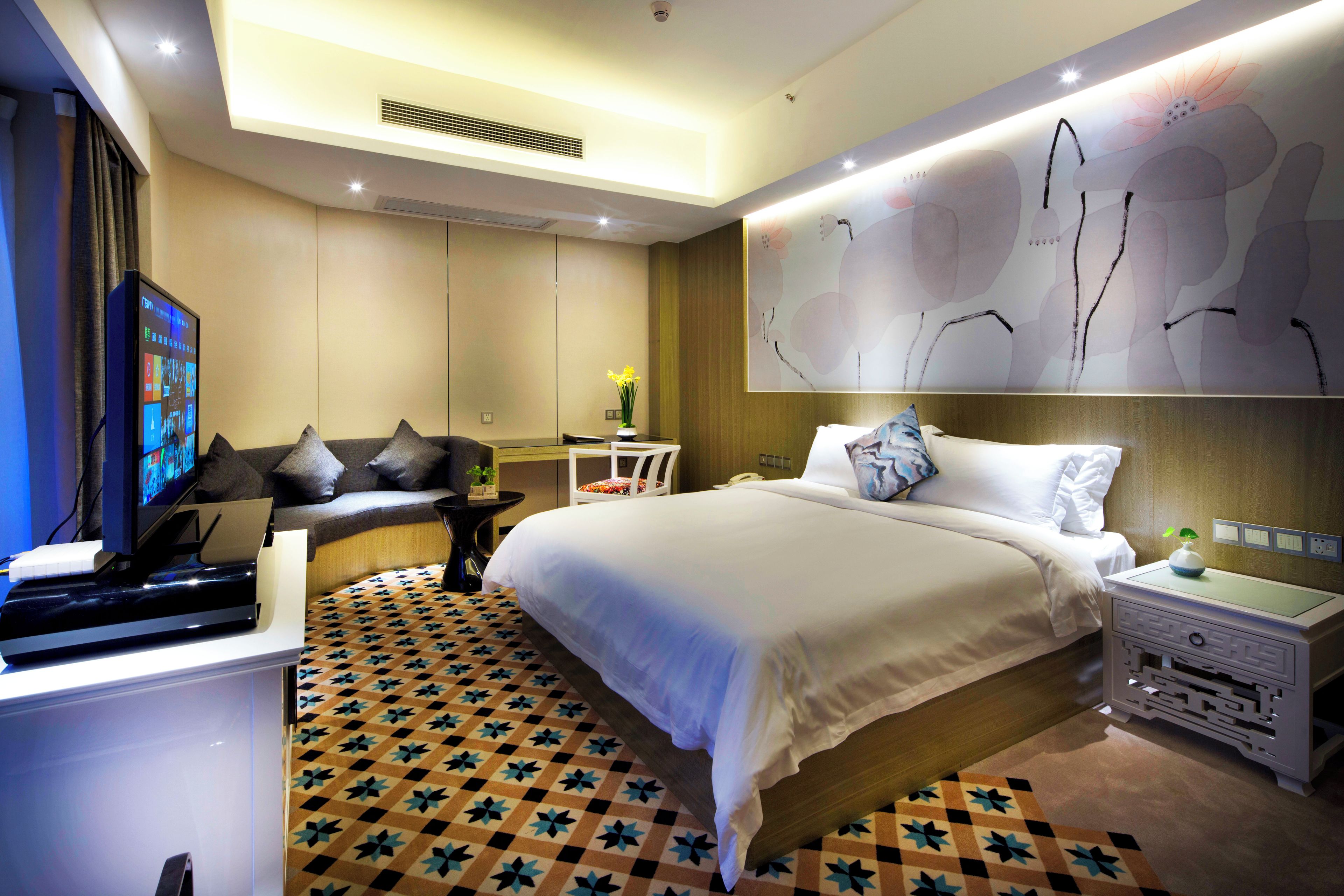 Quarto de hotel moderno com cama, mesa de cabeceira, escrivaninha e uma grande obra de arte na parede.