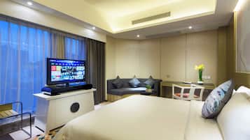 A hotel room with a large bed, a TV on a stand, a desk with a chair, and a sofa.